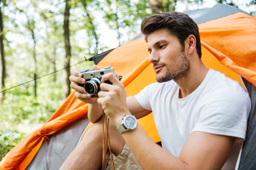 Man tourist sitting and using old vintage camera in forest