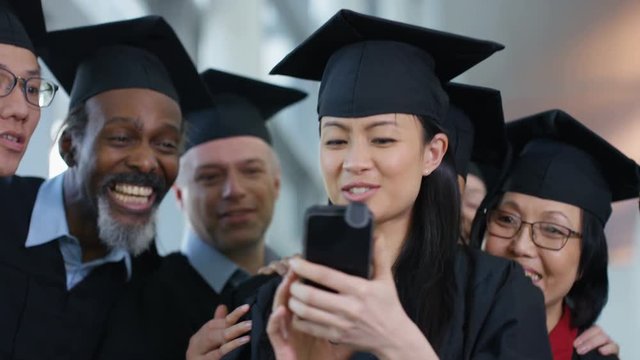  Happy group of mature students on graduation day pose for selfie with mobile 