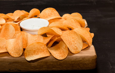 Potato chips with sauce on a black wooden background, selective focus, horizontal, front view 