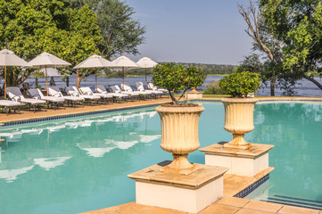 Beautiful Swimming Pool with deck chairs and pottery and Zambezi River in the background