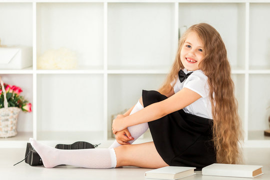 smiling little schoolgirl in school uniform sitting near bookshe