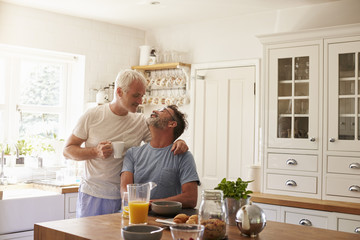 Middle aged gay male couple embracing in their kitchen