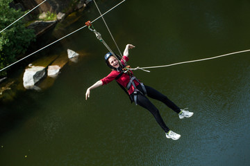 Young perfect woman sliding on a zip line in an adventure park above water.
