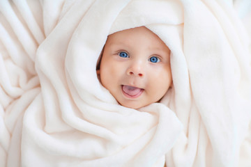 Caucasian baby boy covered with  towel joyfully smiles at camera