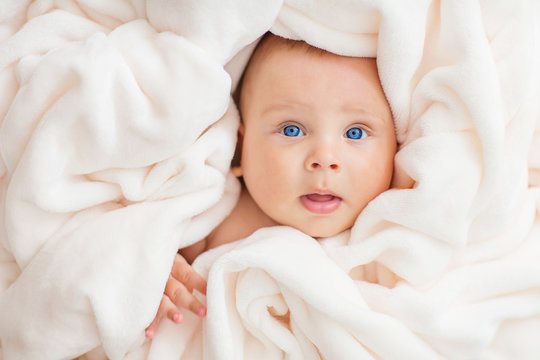 Caucasian baby boy covered with  towel joyfully smiles at camera
