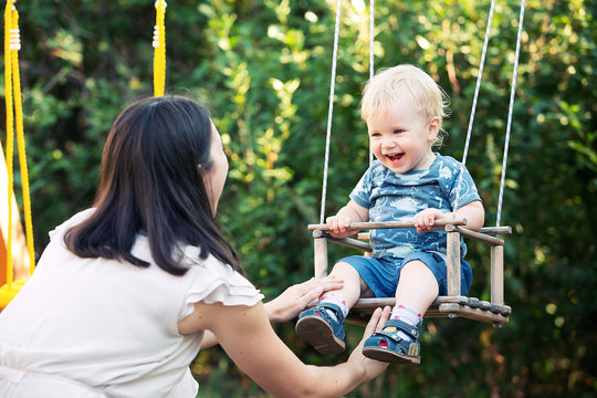 Mom Swinging Her Baby Boy In Swing Outdoor.