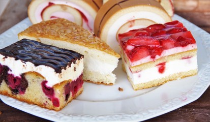 slices of cake with strawberries cherries, almonds and rolls with cream