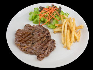 Rib eye steak served with french fries and salads to vegetables isolated on the black background with clipping path