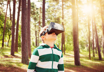 Child standing in the forest in virtual reality glasses. Boy outdoors