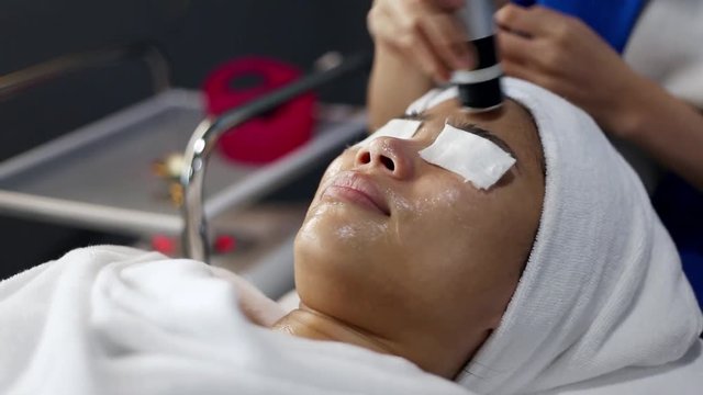 Young Woman getting a cosmetic medicine spa treatment, close up. Beautician hands at work, providing led light skin treatment therapy to a girl face. Special beauty equipment.