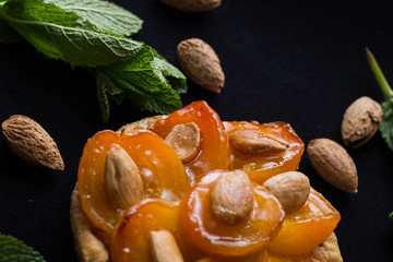Pie with apricot. Traditional french tart with fruits on dark marble background. Decorated almonds and mint leafs. Delicious dessert with copy space closeup.
