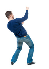 back view of standing man pulling a rope from the top or cling to something.  Rear view people...