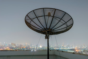 Satellite dish antenna on skycraper in urban area at night.