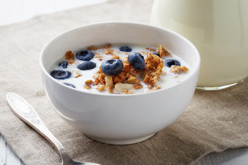 Bowl of whole grain muesli with blueberries and milk on white ta