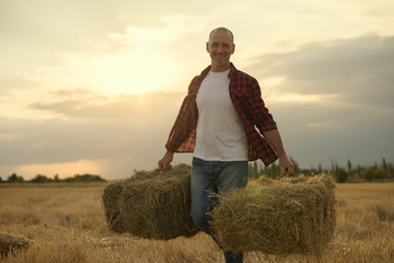 portrait of farmer and harvest. strawbale in hands