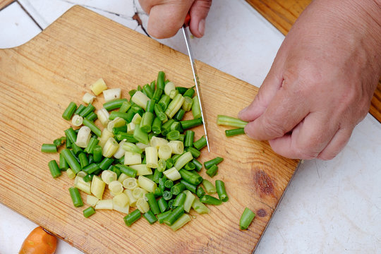 Cut with a knife raw green beans on a wooden board,