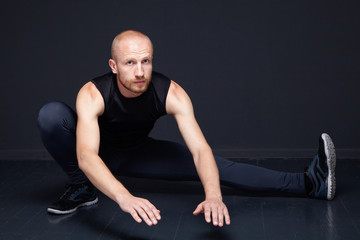 Fototapeta na wymiar Young fitness man performing legs stretching against dark background