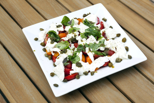 square white plate with caprese salad and capres