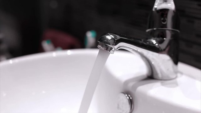 Water flowing on a chrome faucet on an indoor home bathroom