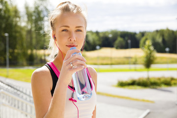 Woman drinks water after running at the countryside