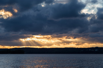 View of dark and dramatic clouds, rays of light and a lake in Finland at sunset in the summer.