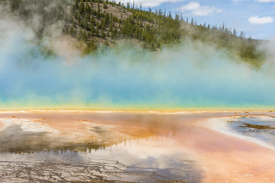 Rising blue steam and mist from hot spring in Midway Geyser basin at Yellowstone National Park with red bacterial patterns