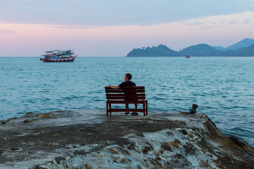 Young man sits lonely at the seaside at dusk.