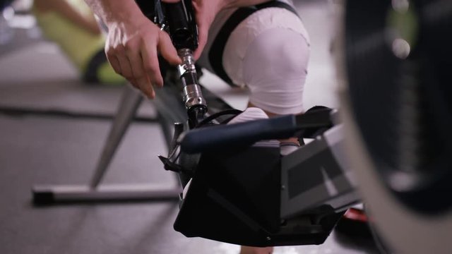  Muscular man with prosthetic leg working out on rowing machine at the gym