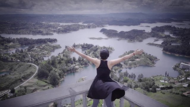 Hispanic woman celebrating her success over a panoramic view of the islands of Guatape, Colombia. Slow motion