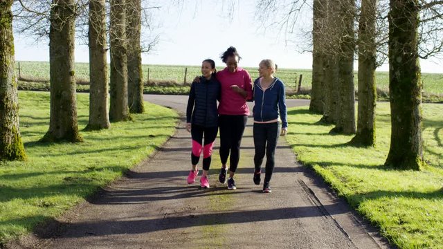  Female friends in fitness clothing walking together outdoors in countryside