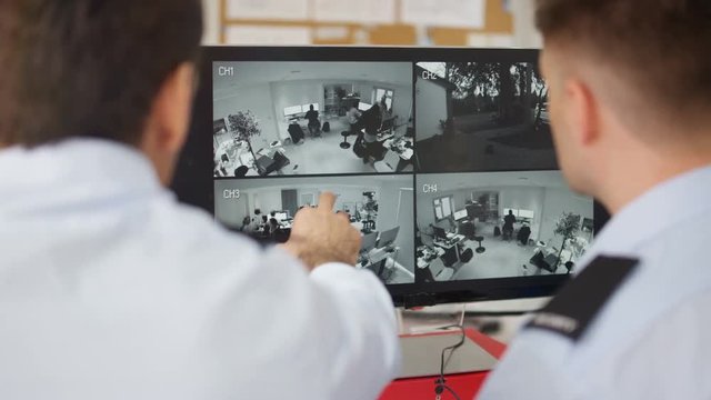  Security workers in system control room looking at CCTV on computer screens. 