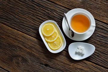 Top view of cup of tea with sugar cube and lemon on wooden table