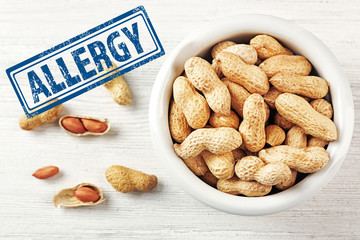 Allergy danger concept. Peanuts in bowl with stamp allergy on white wooden background.