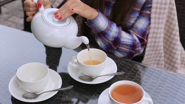 Woman pours tea from a teapot into a cup