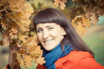 Vintage photo, Smiling woman in autumn park with orange leaves in hands