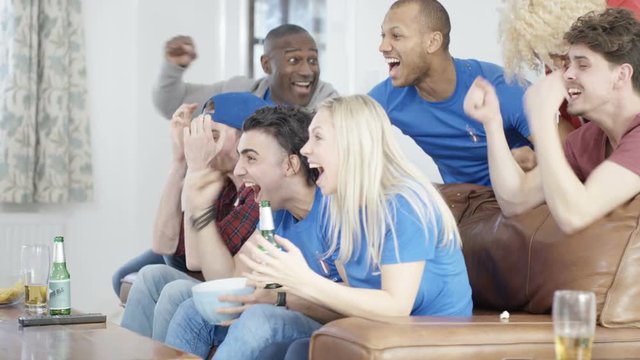 Friends watching sports game on TV celebrate when team scores & spill popcorn