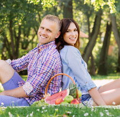 Attractive and cheerful couple staying eating fruits in a park