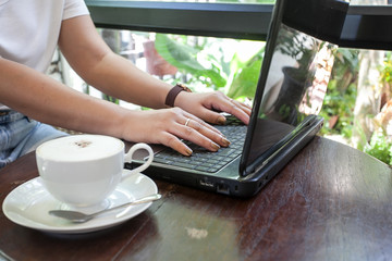 Fototapeta premium Female hand typing on laptop keyboard in coffee shop