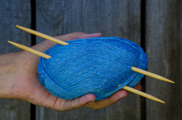 female hand holding a cotton yarn ball with knitting needles