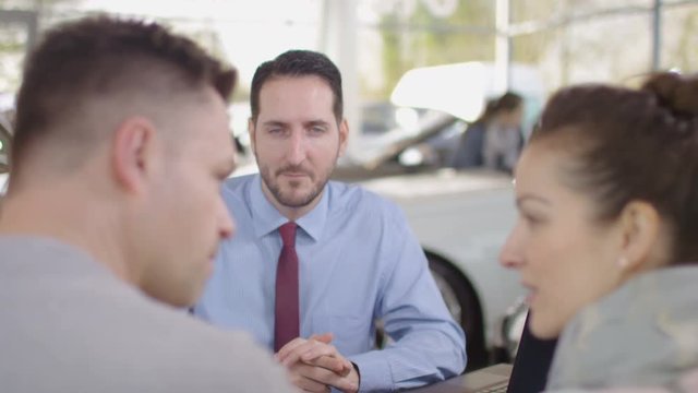  Happy couple in car dealers shake hands with salesman & take key to new car