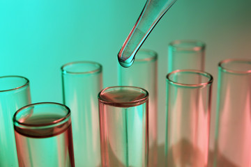 Close up of a pipette dropping a sample into a test tube on green background