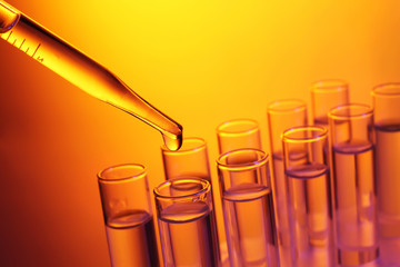 Close up of a pipette dropping a  sample into a test tube on colourful background