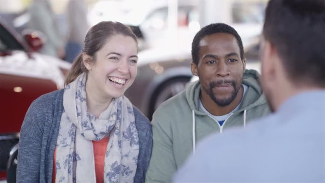  Happy couple negotiating finance terms with salesman in car dealership