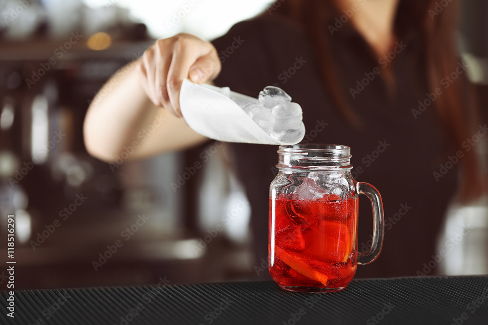 Wall mural woman hands adding ice into cocktail on bar counter