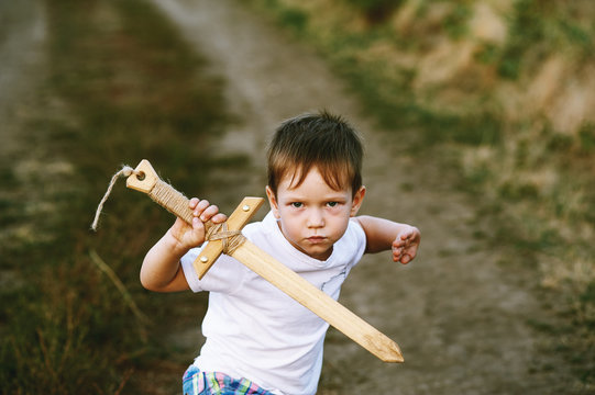 a boy plays with a wooden sword , on a dirt road .