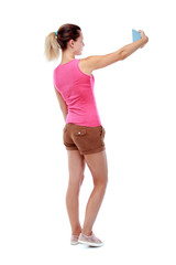 back view of standing young beautiful  woman  using a mobile phone. girl  watching. Rear view people collection.  backside view of person.  Isolated over white background. Sport blond in brown shorts