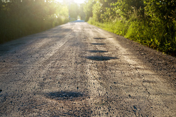 Bumpy dirt road with holes against sunshine in background. Shallow depth of field.