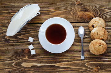 Cup of tea on a wooden table, sugar, spoon, biscuits, napkins, top view