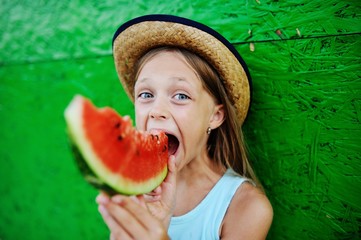 baby girl greedily eating ripe watermelon on a green background