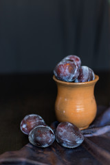 plums on a dark background in a glass vase clay blue summer berry fruits
